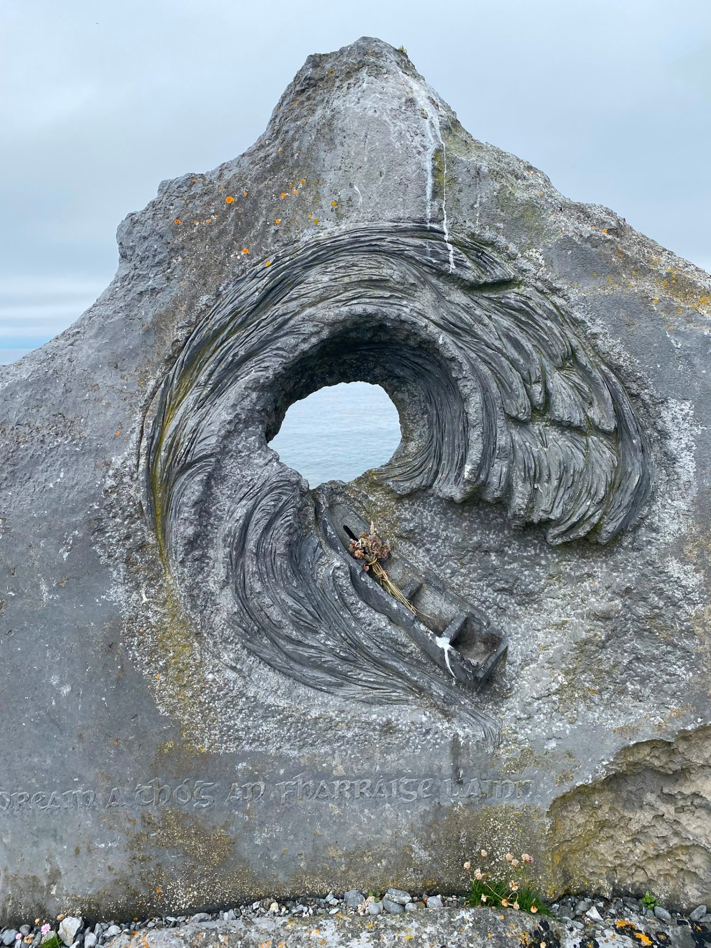 Carved limestone sculpture on the west coast of Ireland, a curling wave enclosing a small boat, inscribed in Irish.